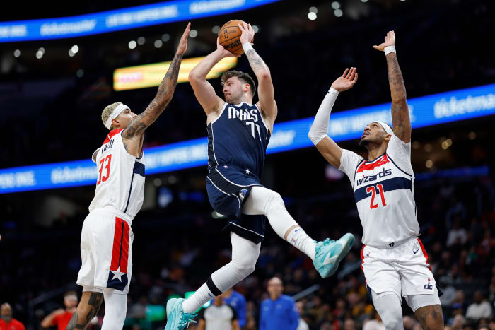 Dallas Mavericks star Luka Doncic throws a pass while being double-teamed by Washington Wizards' Kyle Kuzma and Daniel Gafford.